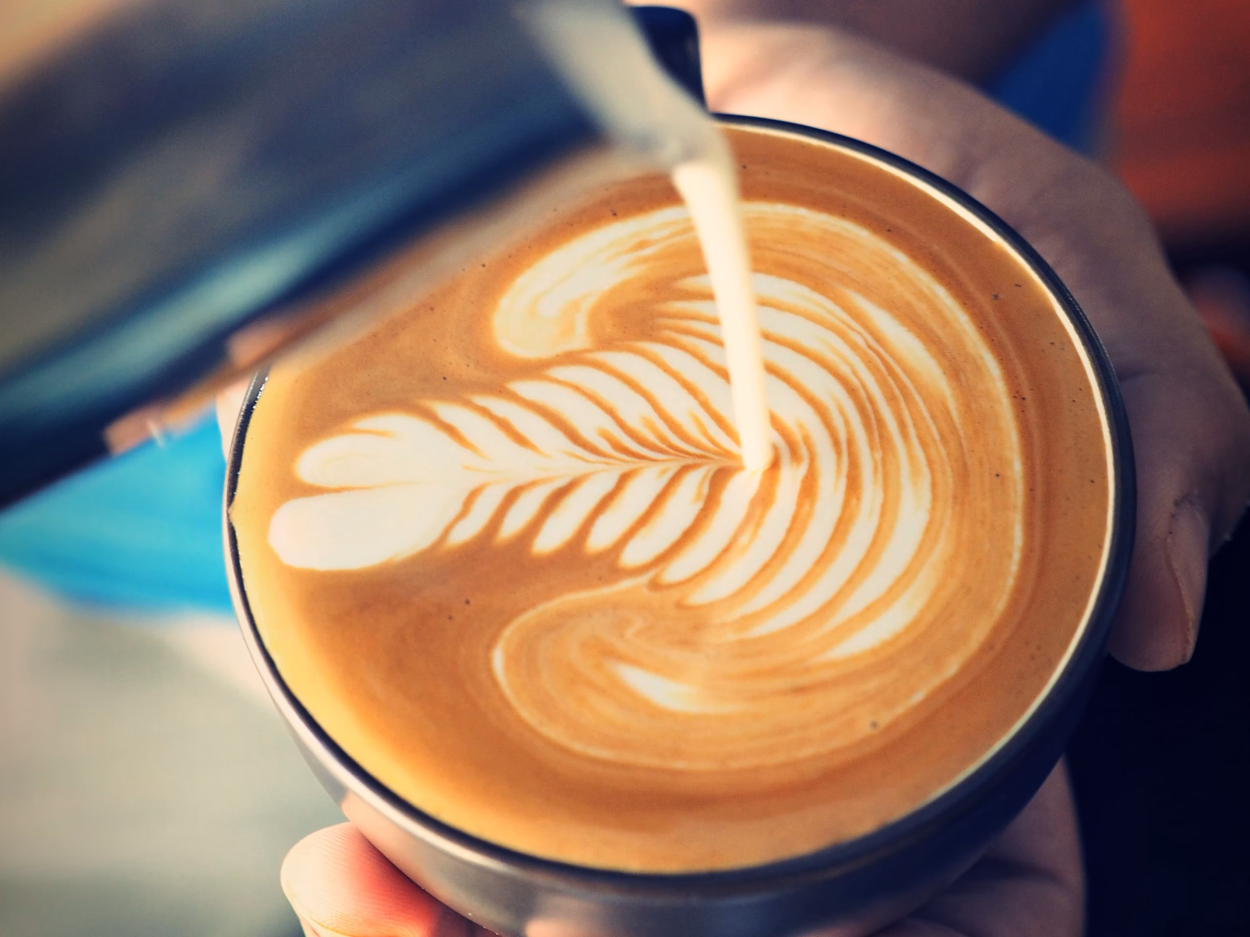 Nahaufnahme von Milch, die in eine Tasse Kaffee mit perfekter Crema gegossen wird.