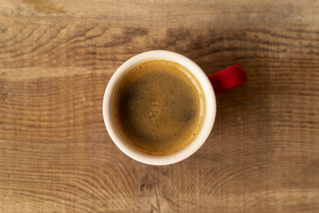 Obere Draufsicht auf eine rote Espressotasse mit Doppio‐Espresso, die auf einer Holzfläche steht. Man sieht die dunkle Crema auf dem Kaffee deutlich.